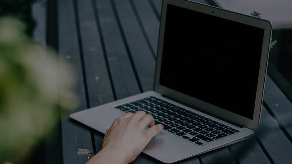 A hand on a laptop outside on a bench